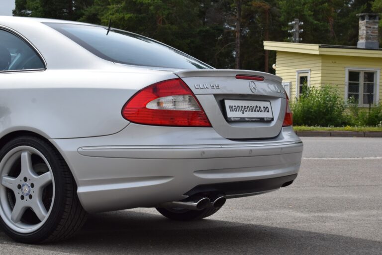 The rear view of a silver Mercedes-Benz CLK 55 AMG parked on a sunny day, with a wangenauto.no license plate and a yellow house in the background.