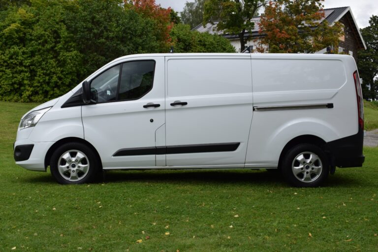 A white cargo van is parked on a grassy area with trees and a building in the background.