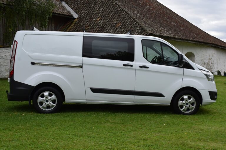 A white cargo van parked on a grassy area in front of an old building with a sloped, tiled roof.