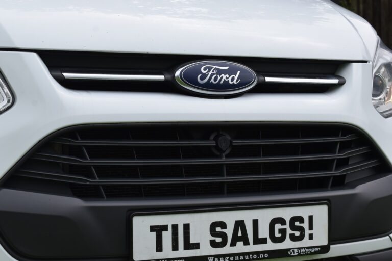 Close-up of a white Ford vehicle's front grille displaying a "TIL SALGS!" sign, indicating it is for sale.