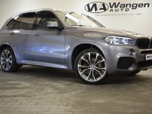 A silver BMW SUV is parked indoors. The vehicle is clean and polished, showcasing its sleek design and alloy wheels. A "Wangen Auto" logo is visible on the wall behind.