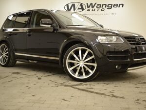 A black Volkswagen SUV parked indoors in front of a wall displaying the "Wangen Auto" logo. The vehicle has large alloy wheels and is well-polished.