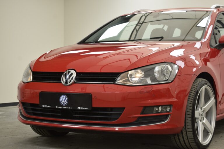 Front view of a red Volkswagen Golf, showing the headlights, front grille with the VW emblem, and part of the front wheel. The car is parked indoors.