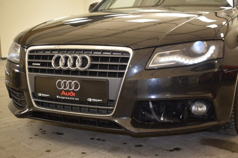 Front view of a black Audi car featuring the iconic four-ring emblem on the grille and illuminated daytime running lights.