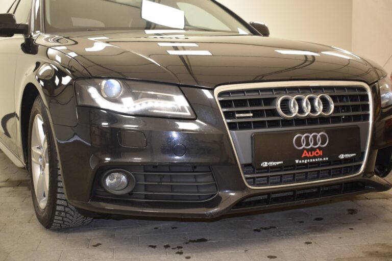 Close-up of the front of a black Audi car, highlighting the grill, headlights, and part of the front bumper. The vehicle is parked indoors.