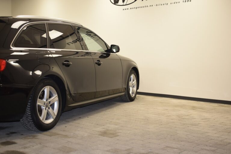 A black car parked indoors on a tiled floor against an off-white wall with a logo.