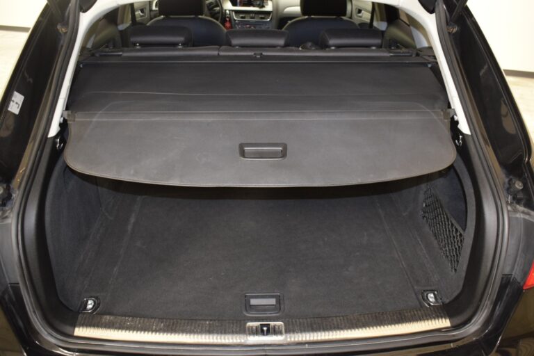 The open trunk of a black vehicle with a cargo cover partially extended, revealing a spacious and empty trunk area.