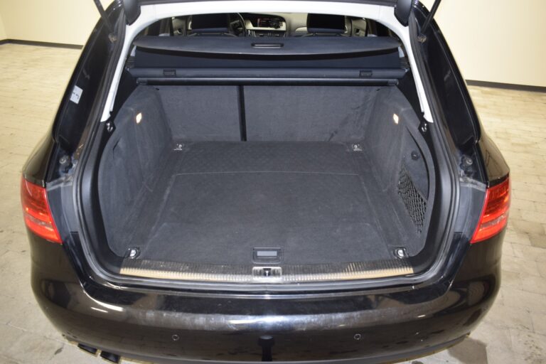 The image shows the open trunk of a black car, revealing a spacious and empty cargo area with carpeted flooring and two small side compartments illuminated by lights.