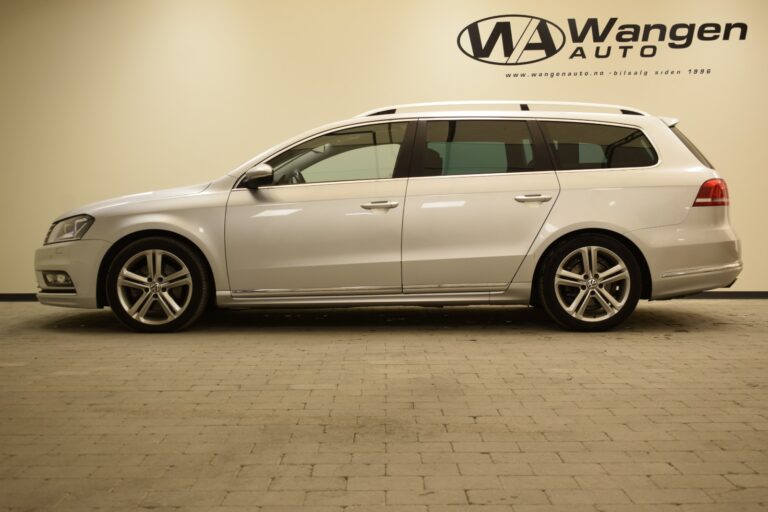 A silver station wagon is parked indoors against a beige wall with the logo and website of Wangen Auto. The vehicle is viewed from the side.