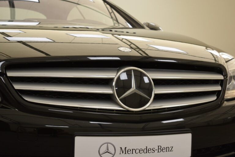 Close-up of the front grille of a black Mercedes-Benz car with the logo prominently displayed. The Mercedes-Benz emblem is centered above the license plate.