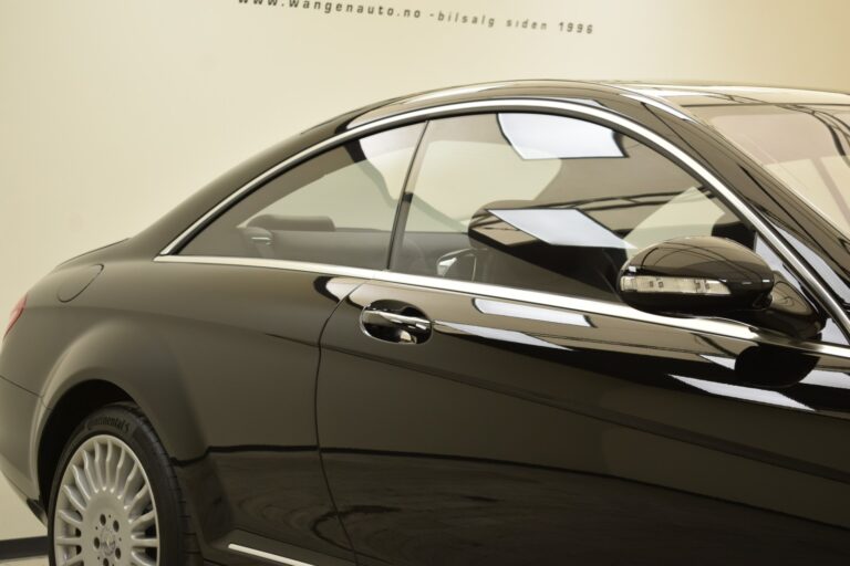 Side view of a shiny black luxury car showing the rear wheel, door, and window on a beige background.