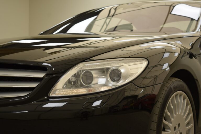 Close-up of the front left side of a black car showcasing its headlight, part of the grille, and the tire.