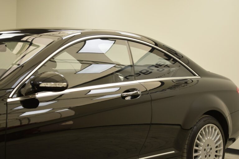 Side view of a black luxury coupe showing the rear window, chrome trim, and a portion of a large alloy wheel.