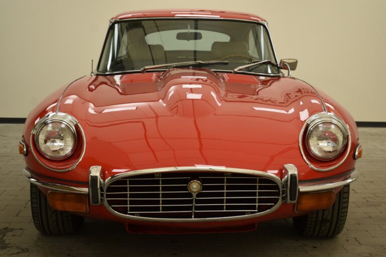 Front view of a classic red sports car featuring a sleek design, round headlights, and a prominent chrome grille.