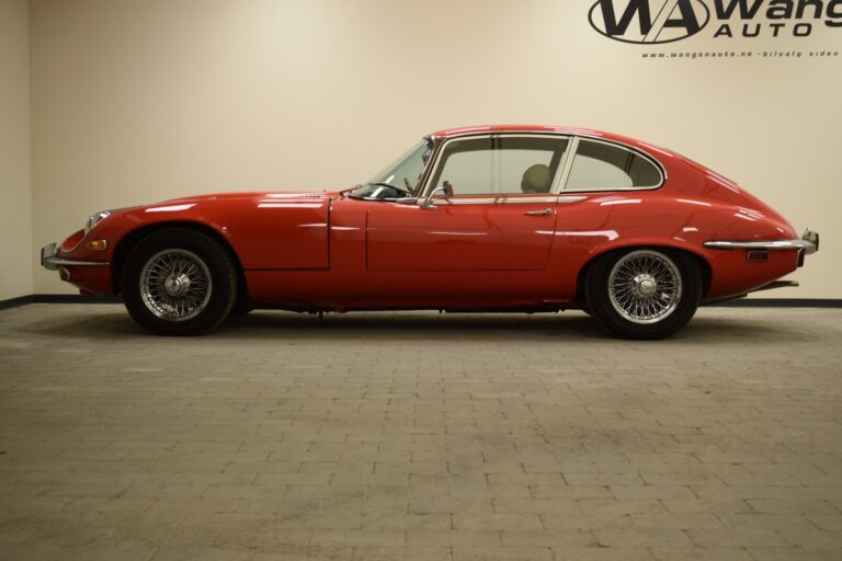 A red classic car with a sleek, curved design is parked indoors on a tiled floor, with a sign for Wang Auto on the beige wall in the background.