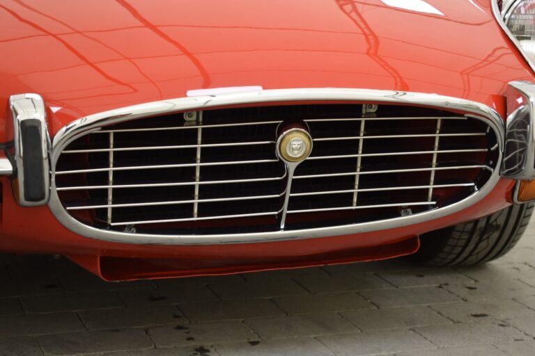 Close-up of the front grille and bumper of a red vintage car with chrome accents.