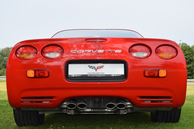 Rear view of a red Corvette sports car parked on grass, displaying the brand logo and dual exhaust pipes.