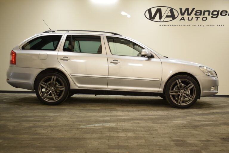 A silver station wagon parked indoors in front of a wall with the "Wanger Auto" logo and website.