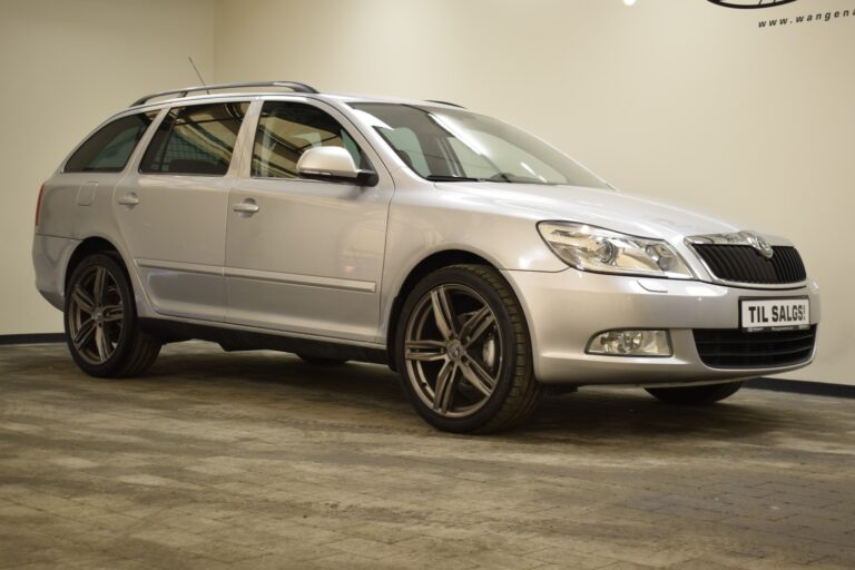 A silver station wagon car is parked in an indoor showroom with a "TIL SALGS" sign on the front license plate.