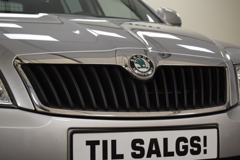 Close-up of a silver car's front grille with the Škoda logo and a "TIL SALGS!" sign, indicating the vehicle is for sale.