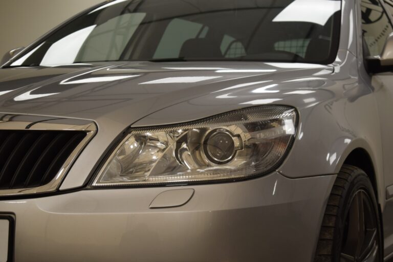 Close-up view of the front left side of a silver car, showcasing the headlight, part of the grille, and the bumper.