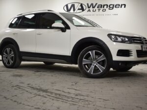 A white SUV is parked indoors on a tiled floor. The backdrop displays the logo and text for Wangen Auto.