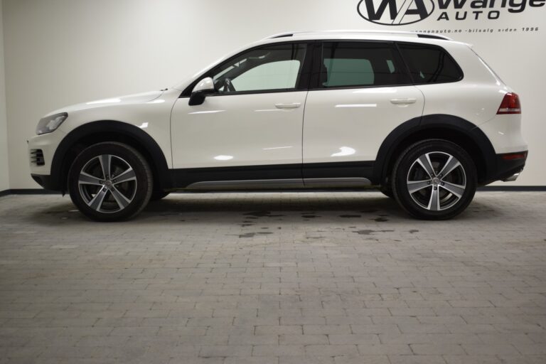 A white SUV is parked indoors on a brick floor. The vehicle is seen from the side, and the setting appears to be a showroom.