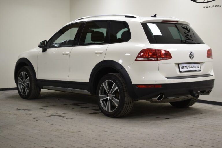 A white Volkswagen SUV is parked indoors against a plain white wall, with dealership information visible in the background.