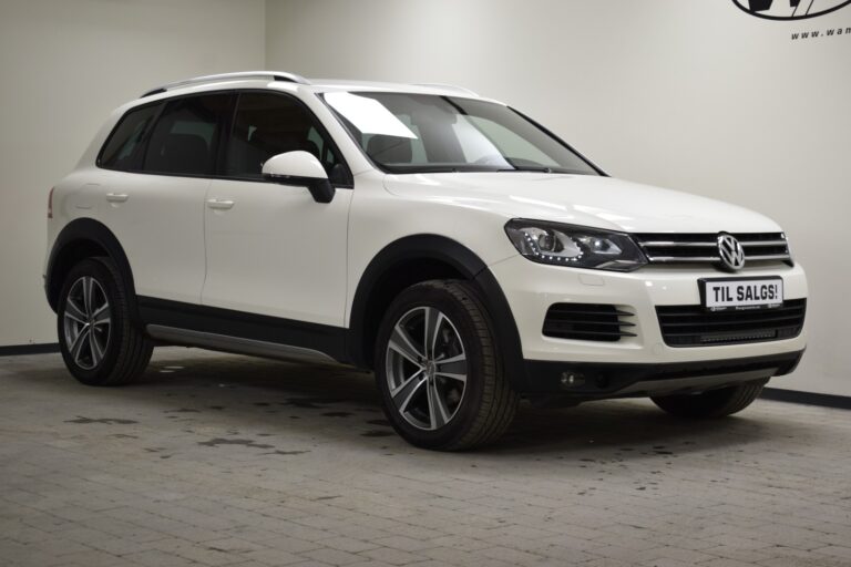 A white Volkswagen SUV parked indoors on a tiled floor with a "TIL SALGS!" sign on the front, indicating it is for sale.