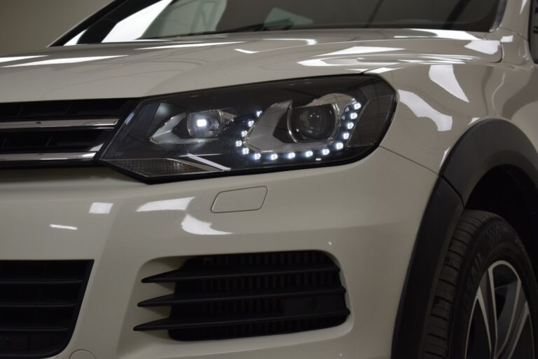 Close-up view of the front left headlight and bumper of a modern white car with LED running lights.