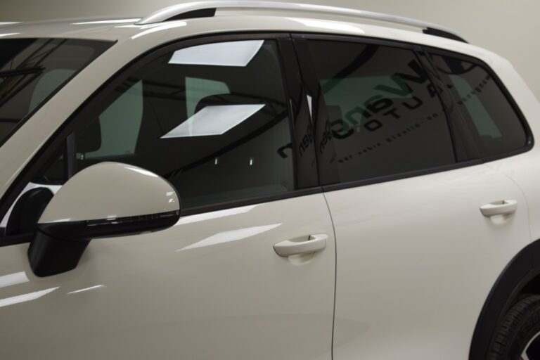 Side view of a white SUV with tinted windows, showing the vehicle's door and side mirror in a well-lit indoor setting.