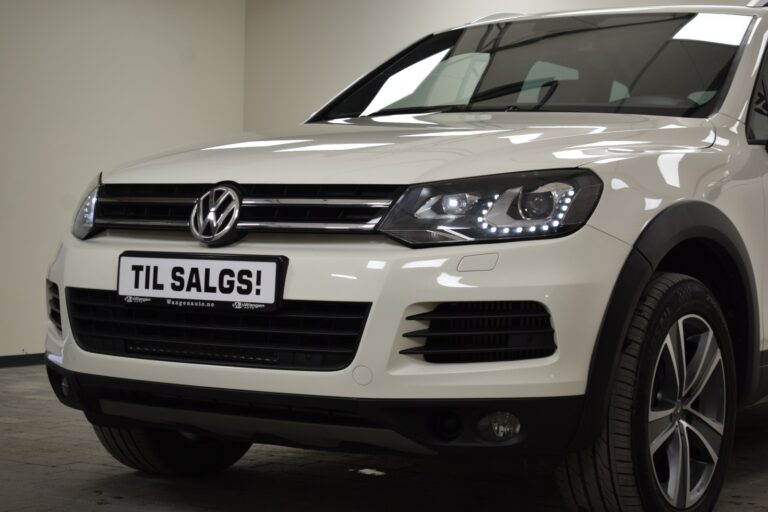 A white Volkswagen SUV parked indoors with a front view. A sign reading "TIL SALGS!" is placed on the front of the car.