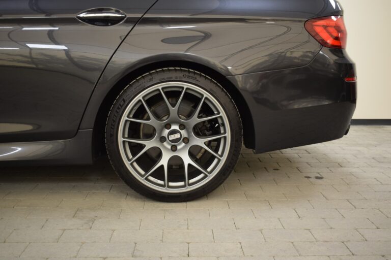 Rear section of a dark gray car showcasing a close-up of its alloy wheel and tire on a concrete surface.