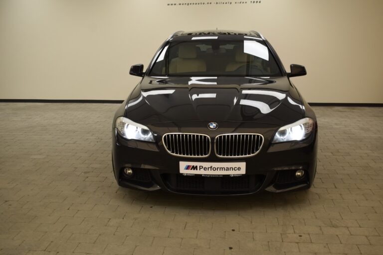 Front view of a black BMW car parked indoors. The car has the headlights on and a plate in front that reads "M Performance".