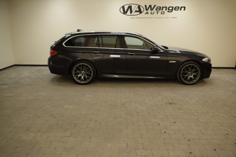 A dark-colored station wagon is parked indoors on a tiled floor. The rear and side walls have the Wangen Auto logo and branding.