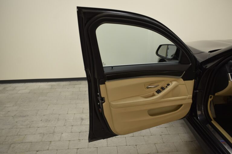 An open black car door exposing the interior, which features light beige upholstery and various control buttons on the armrest, is displayed.