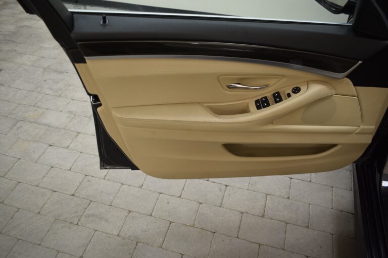 Close-up of an open car door showing the interior detailing on the inside panel, including the handle, control buttons, and beige upholstery.