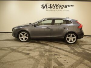 A gray four-door hatchback car is parked inside a showroom with "Wangen Auto" signage on the wall in the background.