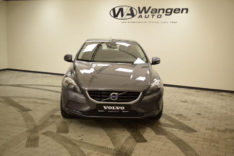 Front view of a gray Volvo sedan displayed in a showroom with "Wangen Auto" signage on the wall behind it.