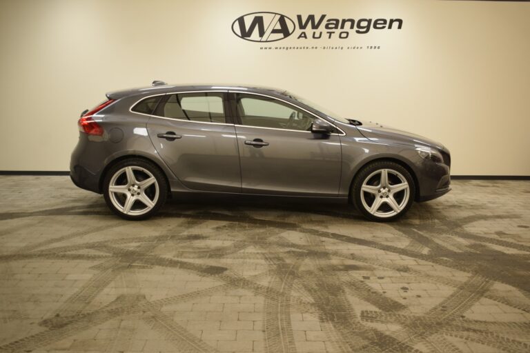 A gray hatchback car is parked indoors on a concrete floor. The wall behind features "Wangen Auto" branding.