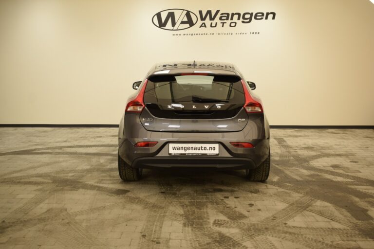 Rear view of a gray Volvo V40 parked indoors at a showroom with beige walls and a logo of Wangen Auto on the wall in front.