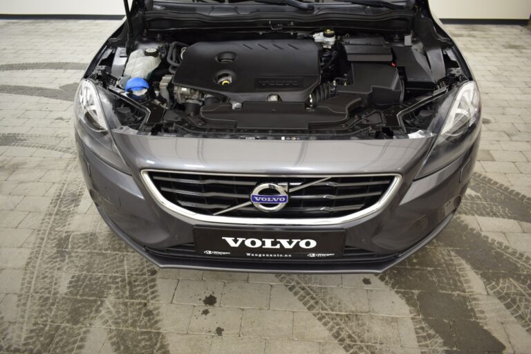 Front view of a gray Volvo car with the hood open, showing the engine. The car is parked on a tiled surface.