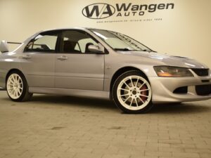 A silver Mitsubishi Lancer Evolution parked indoors with a front-body kit, rear spoiler, and white alloy wheels.