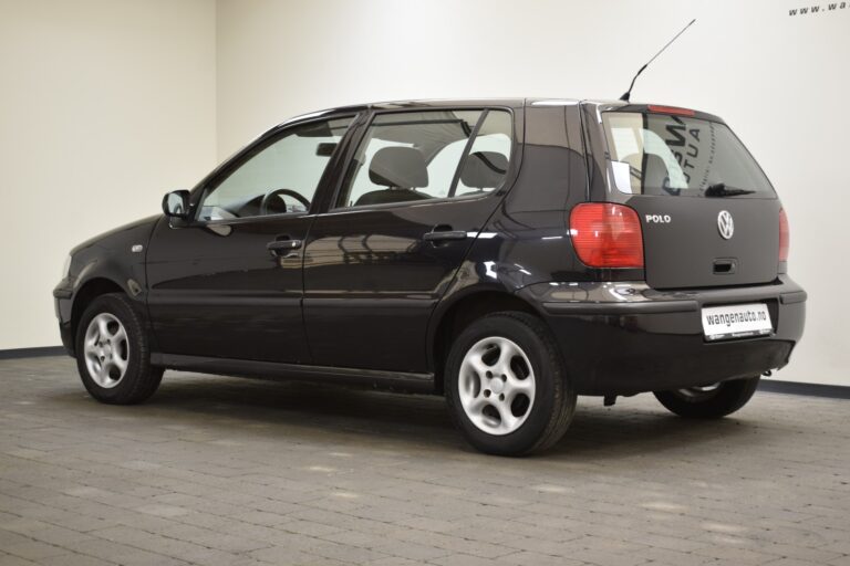 A dark-colored Volkswagen Polo car is parked indoors on a tiled floor, viewed from an angle that shows the rear and left side of the vehicle.