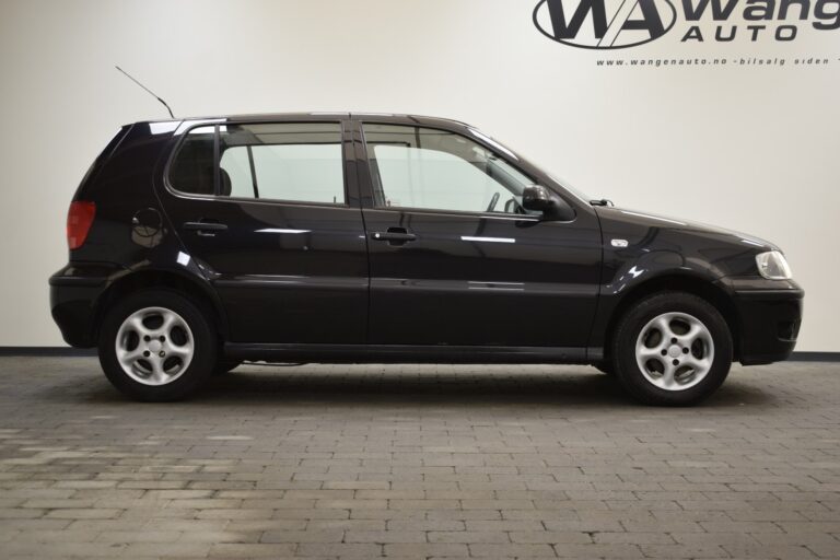 A black 5-door compact car is parked indoors on a grey tiled floor. The wall behind has "Wang Auto" branding.