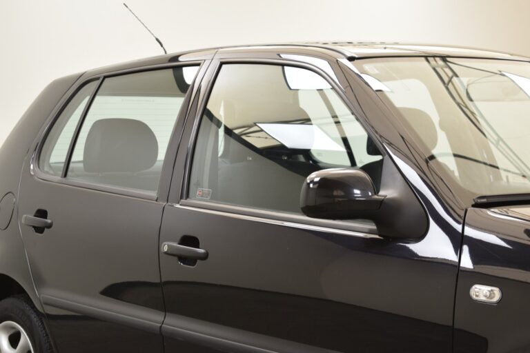 A close-up side view of a black car showing its front and rear passenger side windows, side mirror, and part of the rear passenger door. The car is parked indoors under bright lighting.