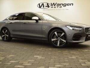 A grey Volvo sedan is parked indoors on a brick floor in front of a wall with the Wangen Auto logo.