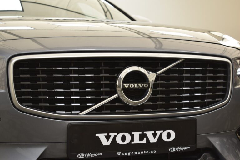 Close-up of a Volvo car front grille displaying the Volvo emblem prominently in the center and a license plate with the Volvo brand name below.