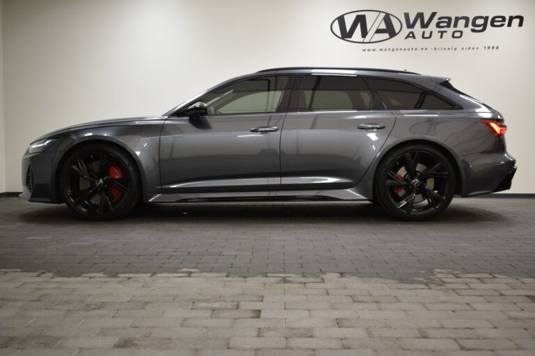 A gray Audi station wagon is parked indoors on a tiled floor, viewed from the side. The Wangen Auto logo and website are visible on the wall in the background.