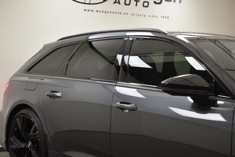 A close-up side view of a dark gray modern car's rear section with tinted windows and black alloy wheels, parked indoors. The background shows a wall with the text "wangenauto.no".